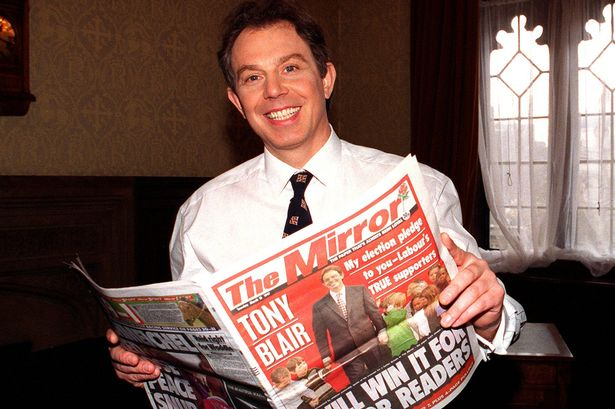 An image of Tony Blair grinning. Blair is pictured holding a copy of The Mirror. The frontpage headline reads 'We Will Win It For Mirror Readers!' and an image of another grinning Blair. 